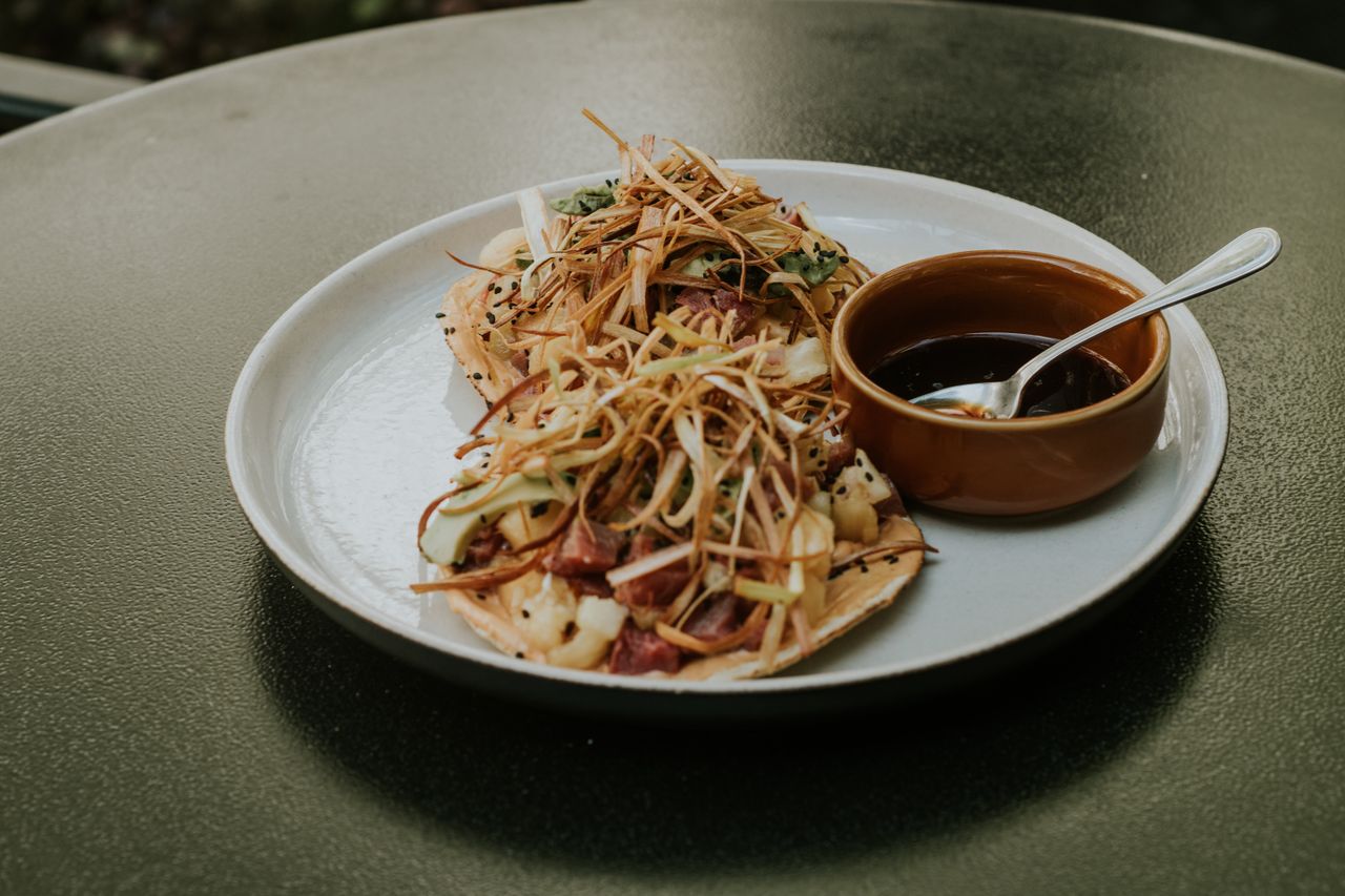 A plate of gourmet tacos topped with crispy ingredients and a side of dipping sauce.